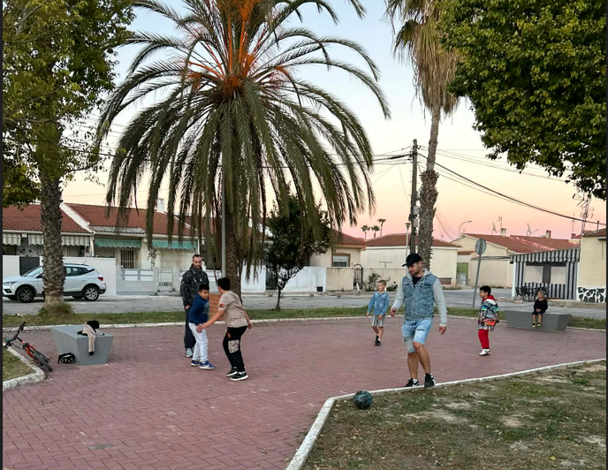 Jalkamäng kivisillutisega platsil lastega, eemal palmipuud